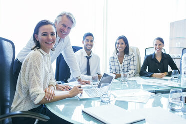 Drei Geschäftsfrauen und zwei Geschäftsmänner sitzen am Konferenztisch und lächeln - CAIF15489