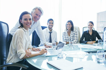 Three businesswomen and two businessmen sitting at conference table, smiling - CAIF15489