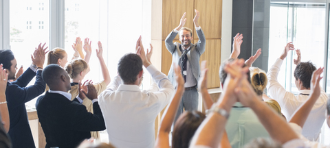 Porträt eines lächelnden Mannes, der vor einem applaudierenden Publikum im Konferenzraum steht, lizenzfreies Stockfoto
