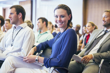 Porträt einer lächelnden jungen Frau, die im Publikum eines Konferenzraums sitzt - CAIF15493