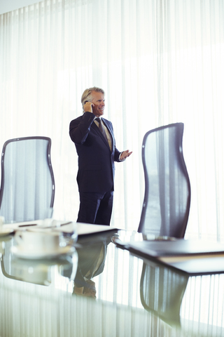 Mann steht in einem Konferenzraum und telefoniert mit seinem Mobiltelefon, lizenzfreies Stockfoto