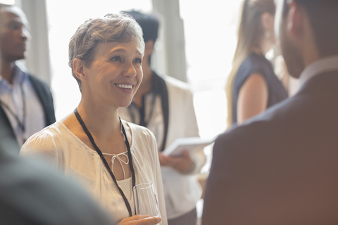 Frau hält Champagnerflöte und unterhält sich mit anderen Leuten auf einem Seminar, lizenzfreies Stockfoto