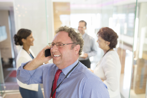 Geschäftsmann, der mit einem Mobiltelefon spricht, Kollegen stehen im Hintergrund, lizenzfreies Stockfoto