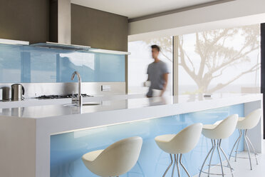 Blurred motion man walking through white and blue modern kitchen - CAIF15528