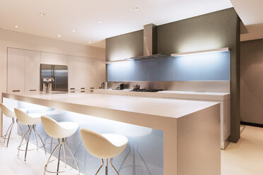 Modern white kitchen with kitchen island and stools illuminated at night - CAIF15546