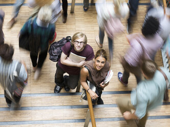 Männliche und weibliche Schüler schauen in die Kamera und stehen in der Pause im Korridor - CAIF15550