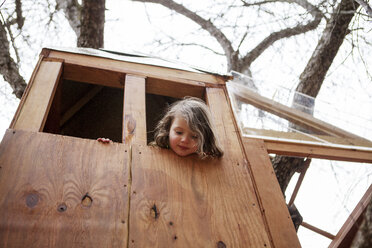 Low angle view of boy looking through window in tree house - CAVF06974