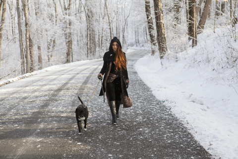 Porträt einer jungen Frau, die im Winter mit ihrem Hund auf der Straße spazieren geht, lizenzfreies Stockfoto