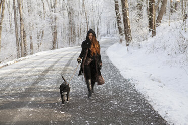 Porträt einer jungen Frau, die im Winter mit ihrem Hund auf der Straße spazieren geht - CAVF06978