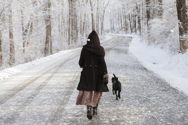 Rückansicht einer Frau, die im Winter mit ihrem Hund auf der Straße spazieren geht - CAVF06979