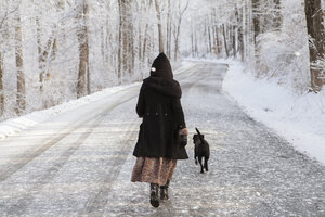 Rear view of woman walking with dog on road during winter - CAVF06979