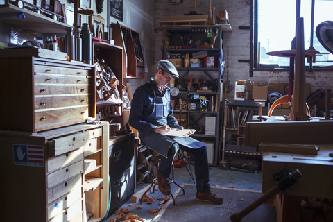 Schreiner in voller Länge beim Lesen eines Dokuments in der Werkstatt, lizenzfreies Stockfoto