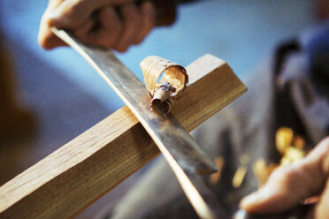 Cropped hands of carpenter shaving wood with drawknife at workshop - CAVF06999