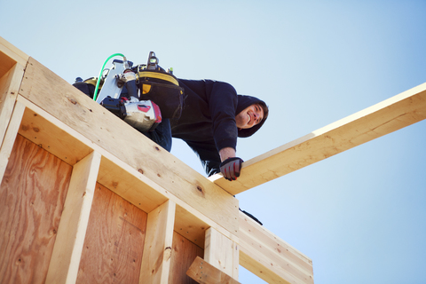 Niedriger Winkel Blick auf lächelnde Arbeiter machen Bau Rahmen gegen klaren blauen Himmel, lizenzfreies Stockfoto