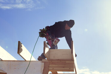 Niedriger Blickwinkel eines Arbeiters mit Bohrmaschine auf einem Dachbalken gegen den Himmel - CAVF07014