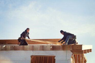 Arbeiter beim Bau von Dachbalken gegen den Himmel an einem sonnigen Tag - CAVF07016