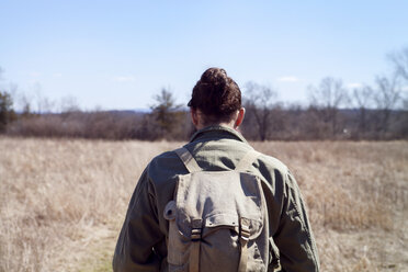 Rear view of male hiker carrying backpack while standing at field during sunny day - CAVF07032