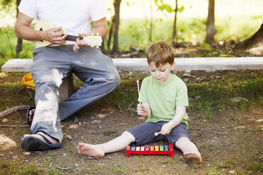 Vater und Sohn spielen auf einem Spielplatz mit Musikinstrumenten - CAVF07035
