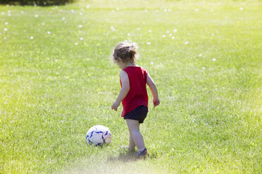 Rückansicht eines Mädchens, das auf einer Wiese Fußball spielt - CAVF07036