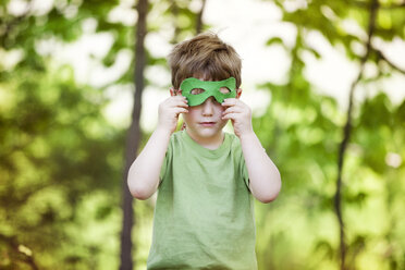Boy wearing eye mask while standing against trees at playground - CAVF07037