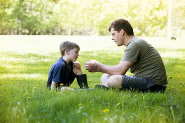 Side view of father and son sitting on grassy field at park - CAVF07051