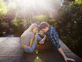 Couple using mobile phone while sitting on roof - CAVF07077