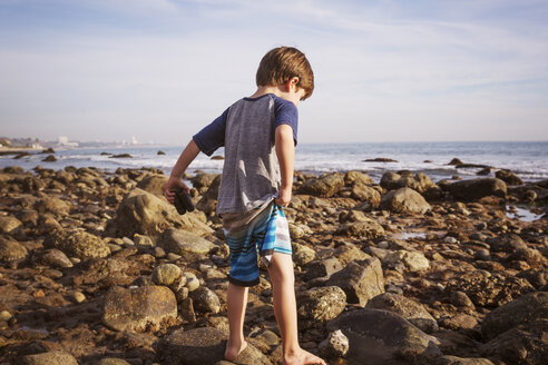 Rückansicht eines Jungen mit Fernglas, der am Strand auf Felsen läuft - CAVF07120