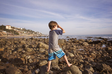 Boy looking through binoculars at beach - CAVF07121