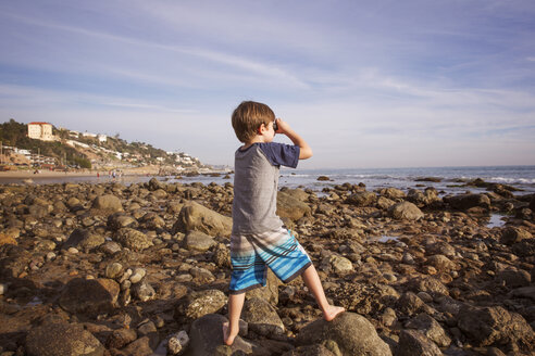 Junge schaut durch ein Fernglas am Strand - CAVF07121