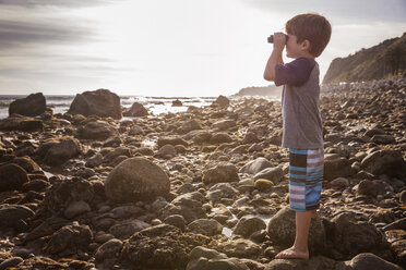 Side view of boy looking through binoculars at beach - CAVF07122