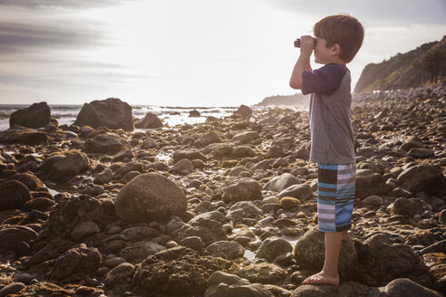 Seitenansicht eines Jungen, der am Strand durch ein Fernglas schaut - CAVF07122