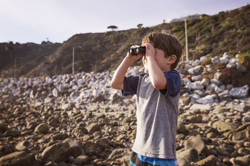 Junge schaut durch ein Fernglas am Strand bei Sonnenuntergang - CAVF07123