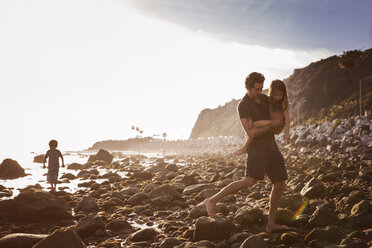 Father carrying daughter while walking on rocks at beach - CAVF07127