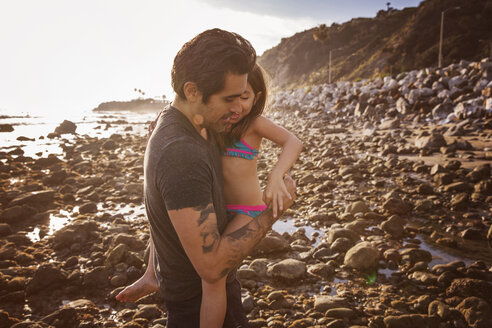 Vater trägt Tochter am Strand bei Sonnenuntergang - CAVF07129