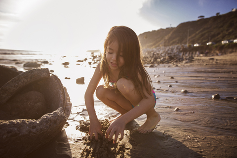 Mädchen spielt im Sand am Strand bei Sonnenuntergang, lizenzfreies Stockfoto