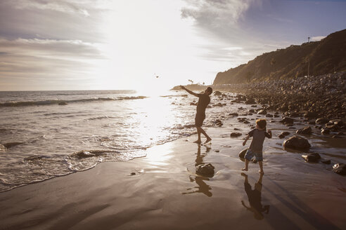 Vater und Sohn werfen bei Sonnenuntergang Steine ins Meer - CAVF07138