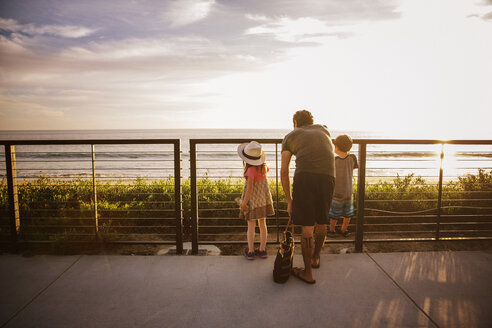 Rückansicht einer Familie, die während des Sonnenuntergangs an der Reling steht und auf das Meer blickt - CAVF07148