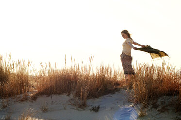 Woman holding scarf while standing on sand against clear sky - CAVF07168