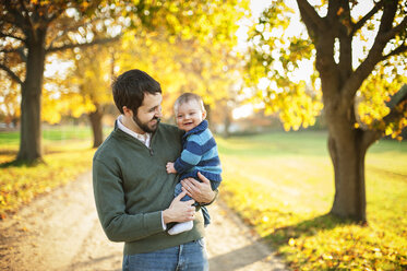 Cheerful father carrying son while standing in park - CAVF07232