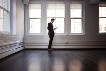 Businessman using tablet while standing by window at office - CAVF07345