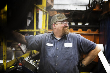 Arbeiter mit Hand an der Hüfte, der wegschaut, während er an einer Maschine in der Metallindustrie steht - CAVF07405