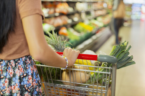Close up of woman pushing full shopping cart in grocery store - CAIF15564