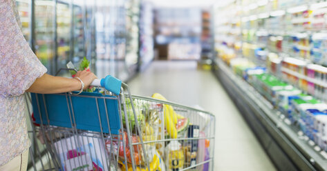 Woman pushing full shopping cart in grocery store - CAIF15617