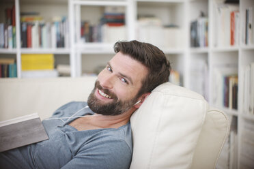 Lächelnder Mann beim Musikhören auf dem Sofa - CAIF15651