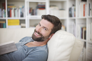 Smiling man listening to music on sofa - CAIF15651