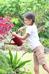 Girl watering plants in garden with red watering can - CAIF15719