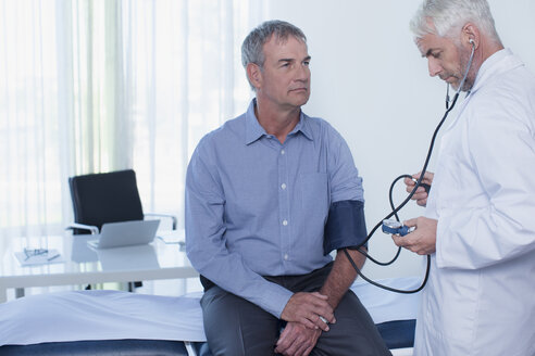 Älterer Arzt, der den Blutdruck eines Patienten im Büro misst - CAIF15728