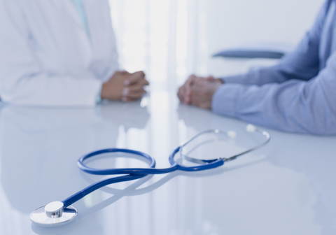 Stethoscope on white desk in doctor's office, female doctor and patient sitting in background stock photo