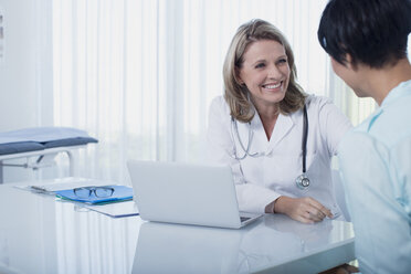 Lächelnde Ärztin und Frau am Schreibtisch sitzend im Büro - CAIF15738