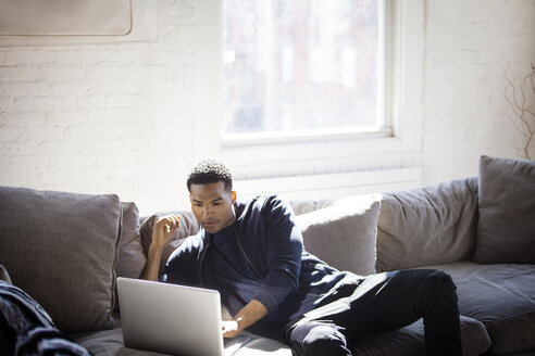 Mann benutzt Laptop, während er zu Hause auf dem Sofa sitzt - CAVF07425